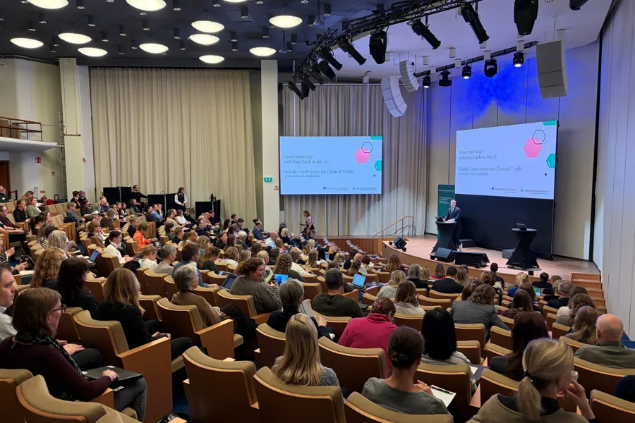 Bilde fra møtesalen: Publikum, konferansier, scene og skjerm